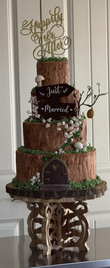 Rustic tiered wedding cake with handcrafted fondant wood-grain details, flowers, greenery, and woodland accents.