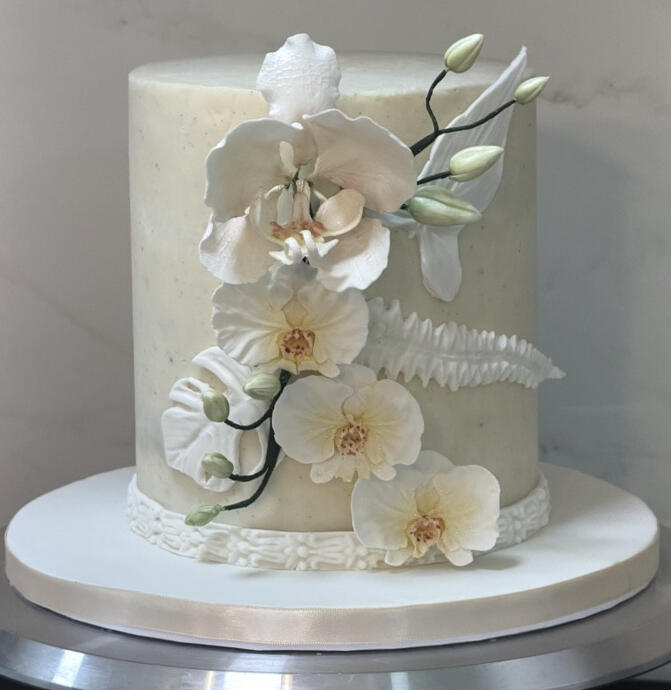Elegant white custom cake decorated with handcrafted white orchids and delicate floral details