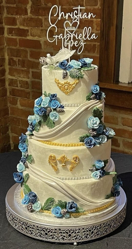 Elegant tiered wedding cake decorated with handcrafted blue roses, gold accents, and ornate detailing.