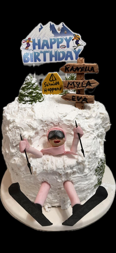 White buttercream ski-themed cake with a handcrafted fondant skier, snowy mountain details, and personalized fondant trail signs.