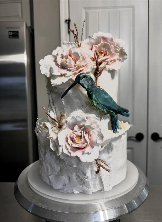 Hummingbird & Sugar Flower Cake Elegant white cake with handmade sugar flowers, edible lace, and a handcrafted gum paste and fondant hummingbird.