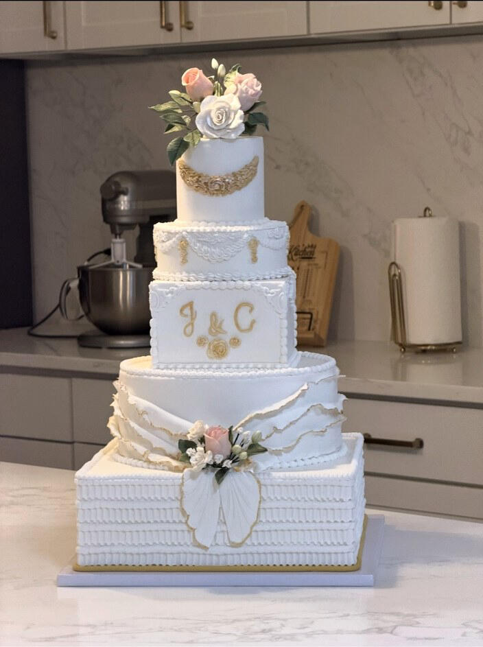 Luxury Custom Wedding Cake Five-tier luxury white wedding cake with handcrafted ruffles, pearl and champagne-gold details, and handmade sugar flowers in soft pink and white.